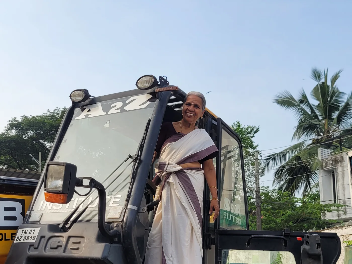 Radhamani Amma beside an A2Z Institute JCB backhoe loader in Kochi, Kerala